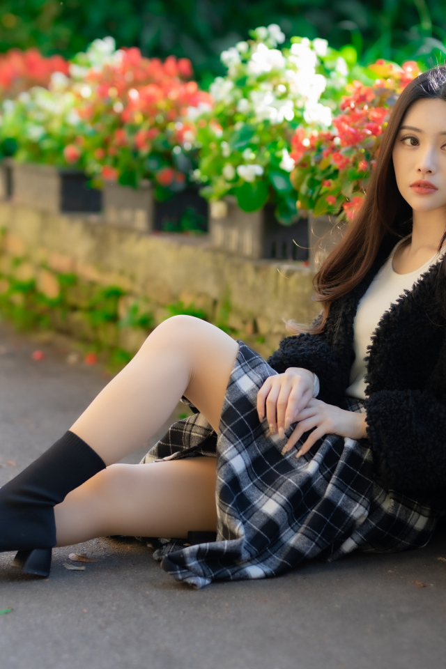 Азиатка сидит на асфальте у цветов