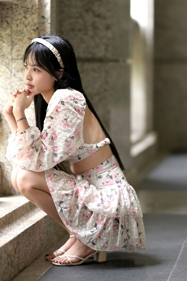 Красивая девушка азиатка в костюме сидит у стены