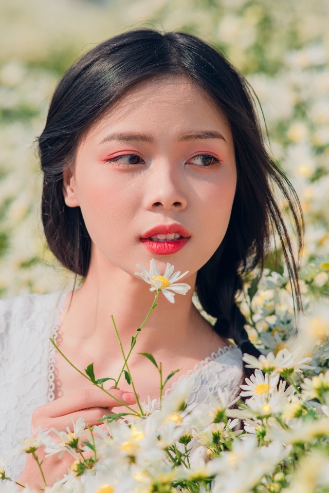 Красивая девушка азиатка на поле с белыми ромашками