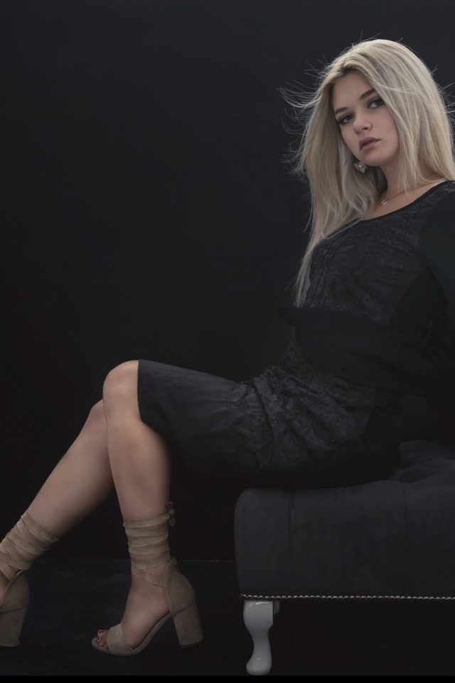 Красивая девушка в черном платье сидит на кресле