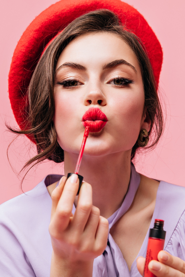 Красивая девушка в красном берете красит губы