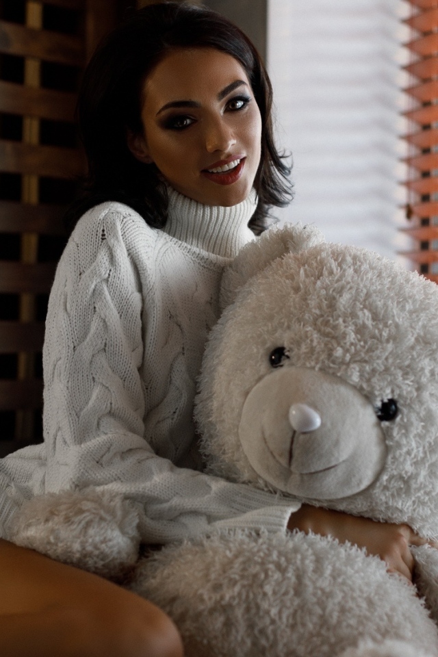 Красивая девушка в свитере с медведем у окна