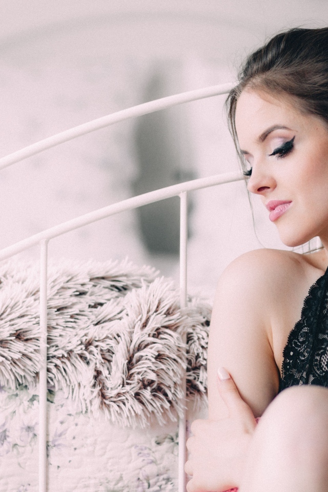 Красивая девушка сидит на полу у кровати 