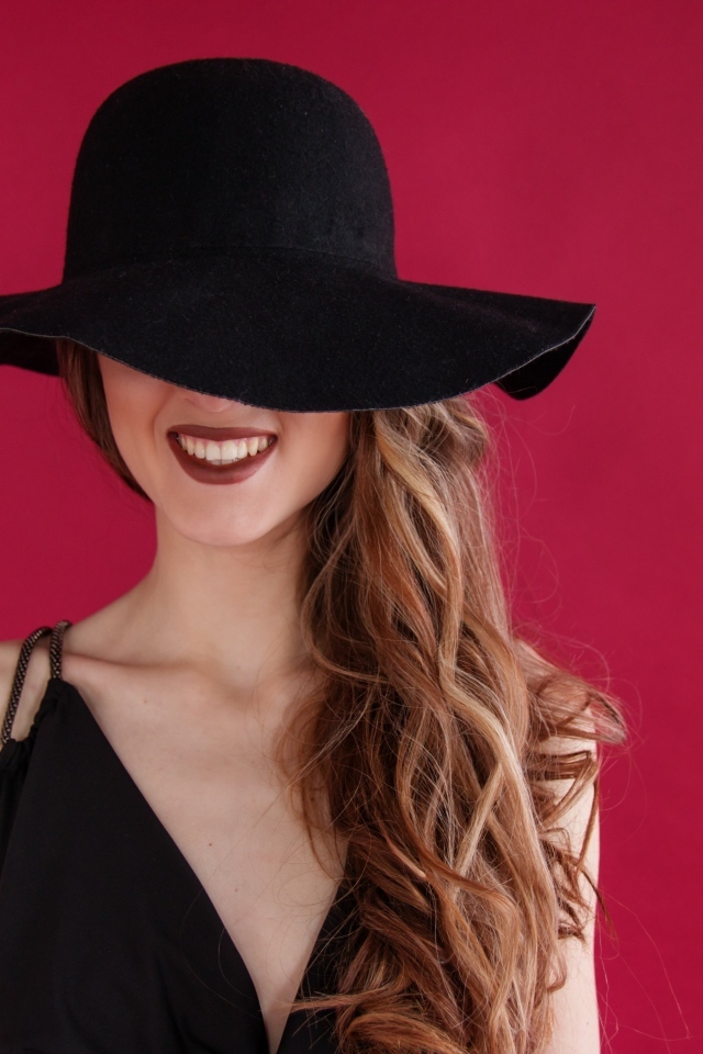 Черная шляпа на лице у девушки на розовом фоне