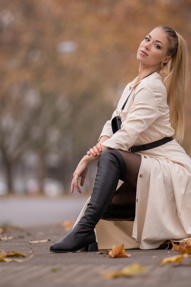 Девушка блондинка сидит в пальто в парке