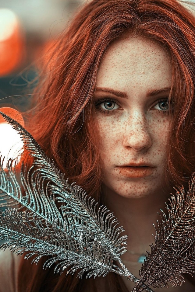 Яркая рыжеволосая девушка с перьями в руках