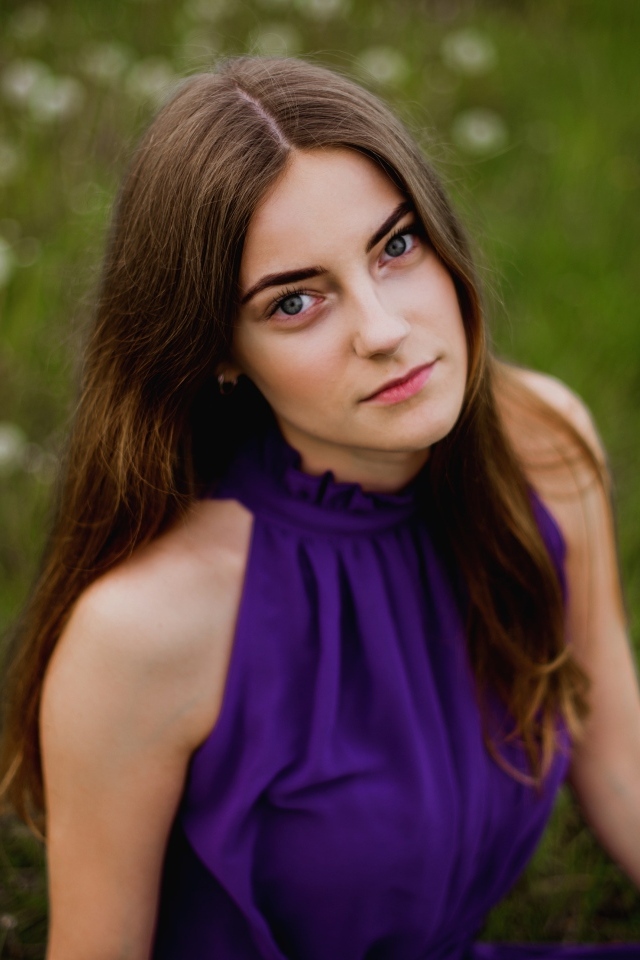 Милая девушка в фиолетовом платье сидит на траве