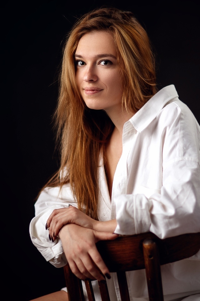 Милая девушка в белой рубашке сидит на стуле