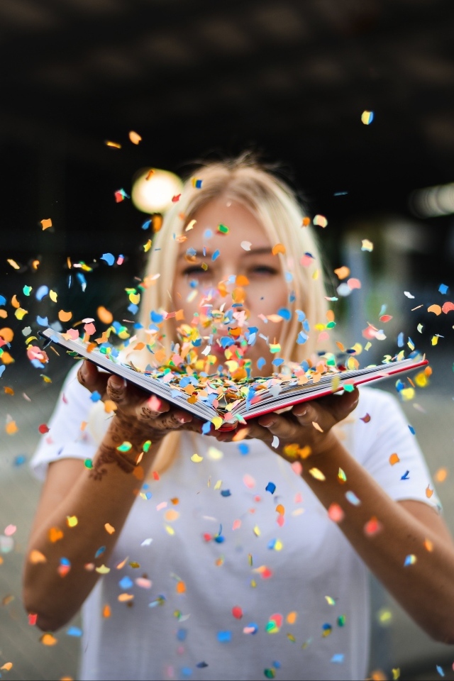 Девушка сдувает конфетти с книги 