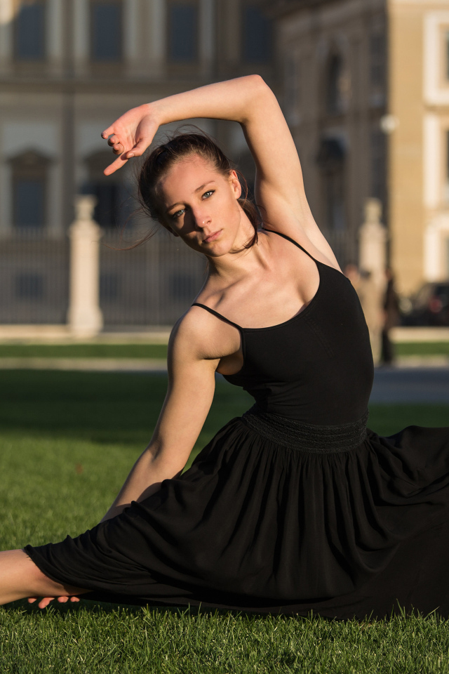 Девушка гимнастка в черном платье на зеленой траве