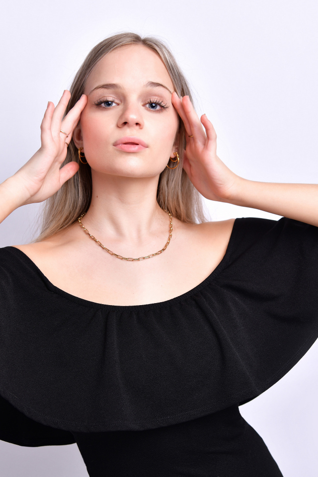 Девушка в черном платье с руками у головы на белом фоне