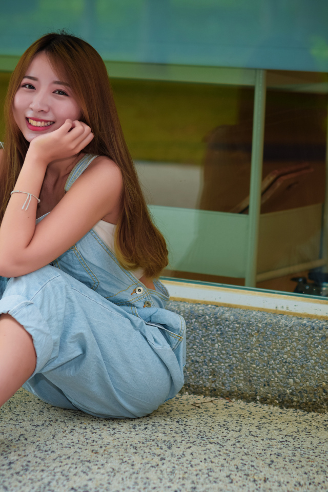 Девушка в джинсовом комбинезоне сидит на полу