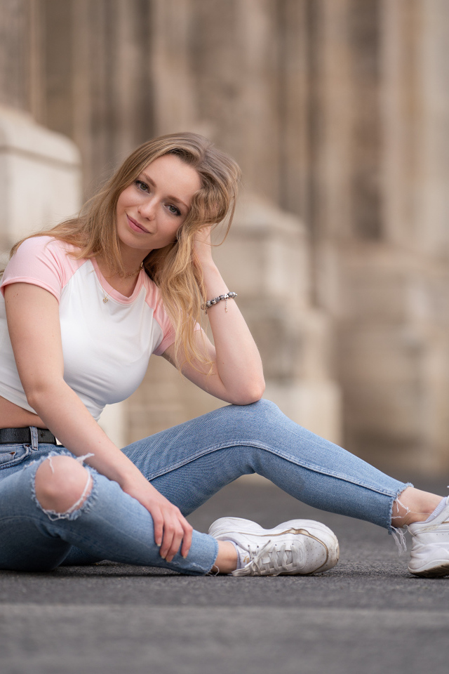 Девушка в рваных джинсах сидит на асфальте