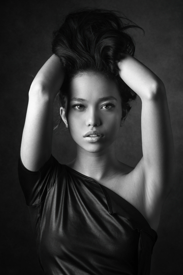 Девушка модель с руками в волосах  у стены