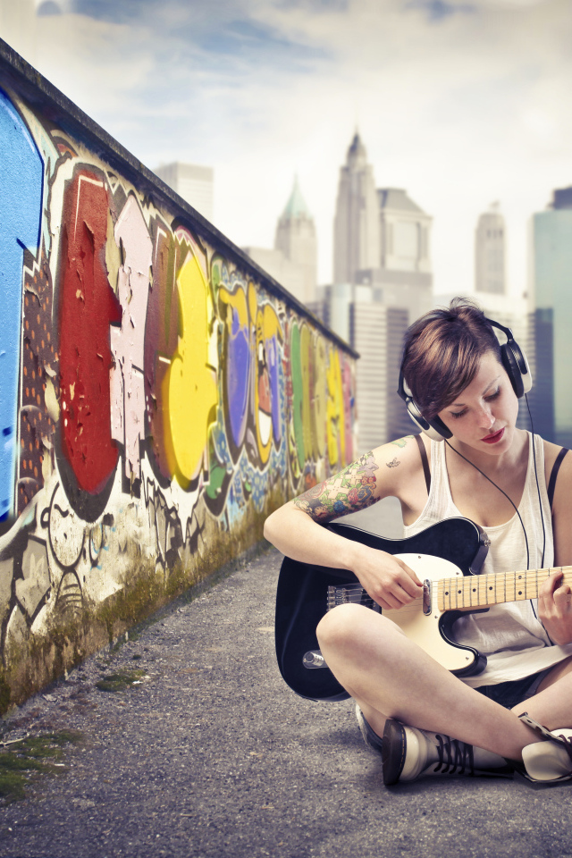 Девушка с гитарой сидит у стены