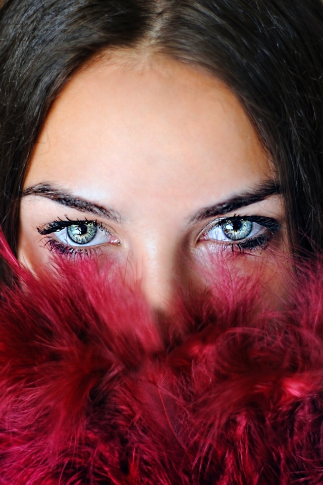 Девушка с красивыми глазами закрыла лицо красными перьями