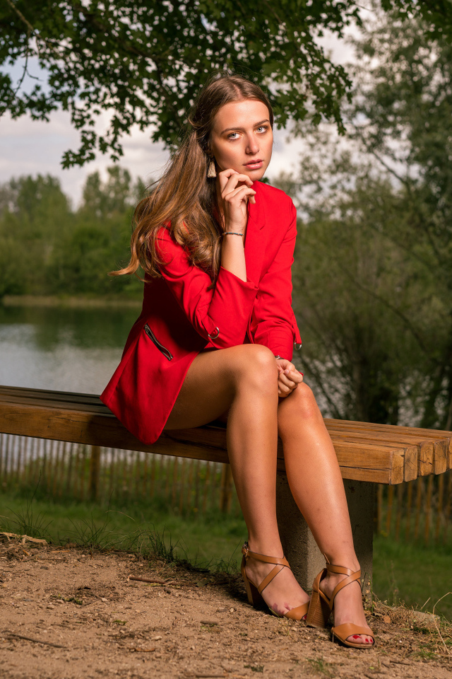 Грустная девушка в красном пальто сидит на лавке