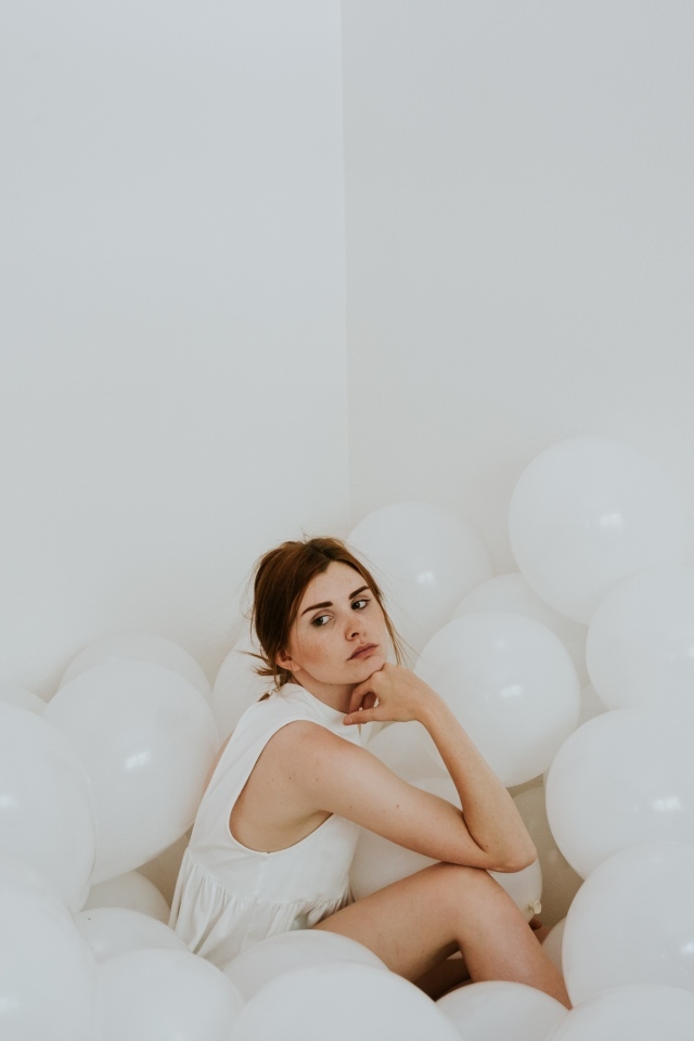 Грустная девушка сидит в белых воздушных шариках