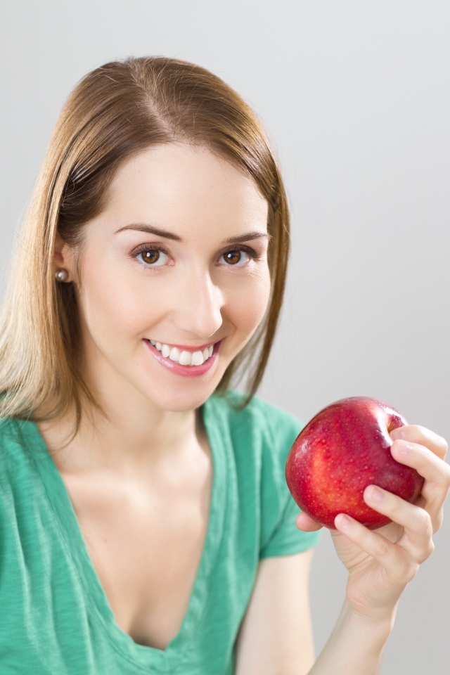 Улыбающаяся девушка с красным яблоком в руках