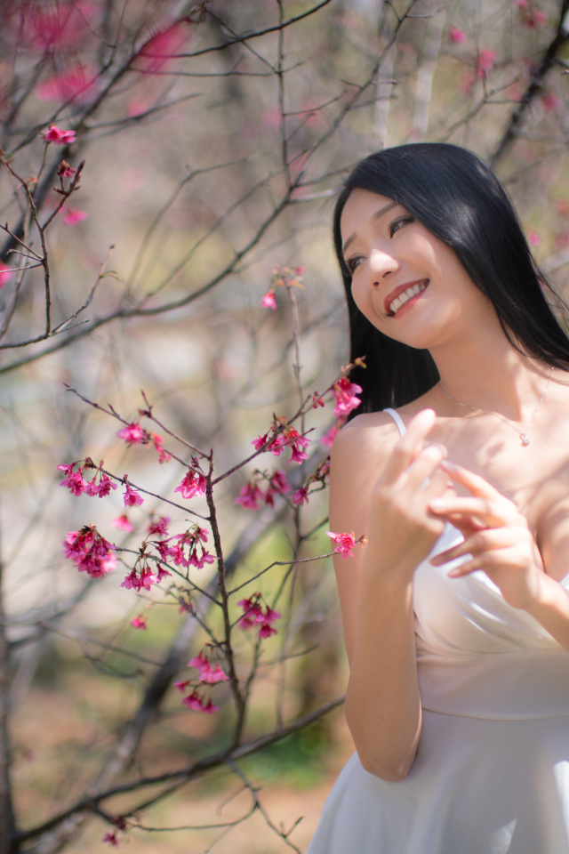 Улыбающаяся девушка в белом платье у дерева с цветами