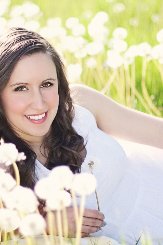 Улыбающаяся девушка лежит на поле с одуванчиками