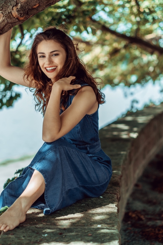 Улыбающаяся девушки сидит у дерева