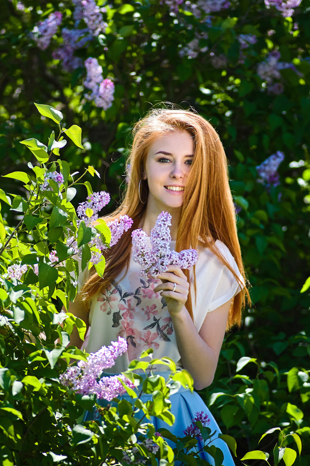 Улыбающаяся девушка стоит у куста сирени