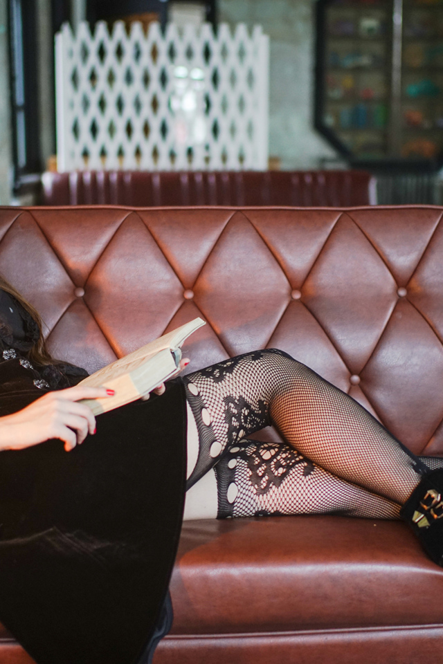 Молодая девушка читает книгу на кожаном диване