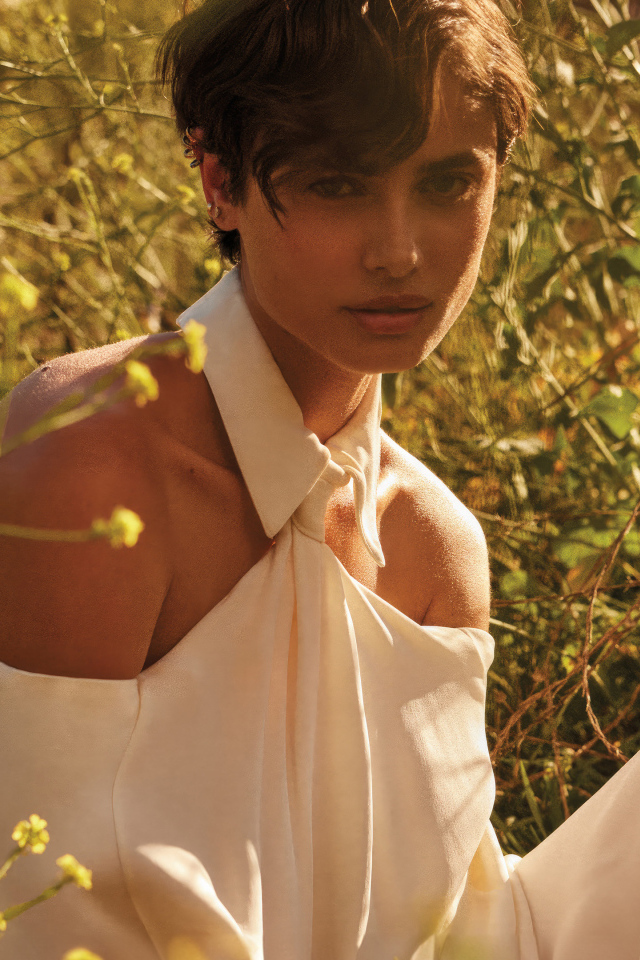 Модель Тейлор Хилл в белом наряде сидит на траве