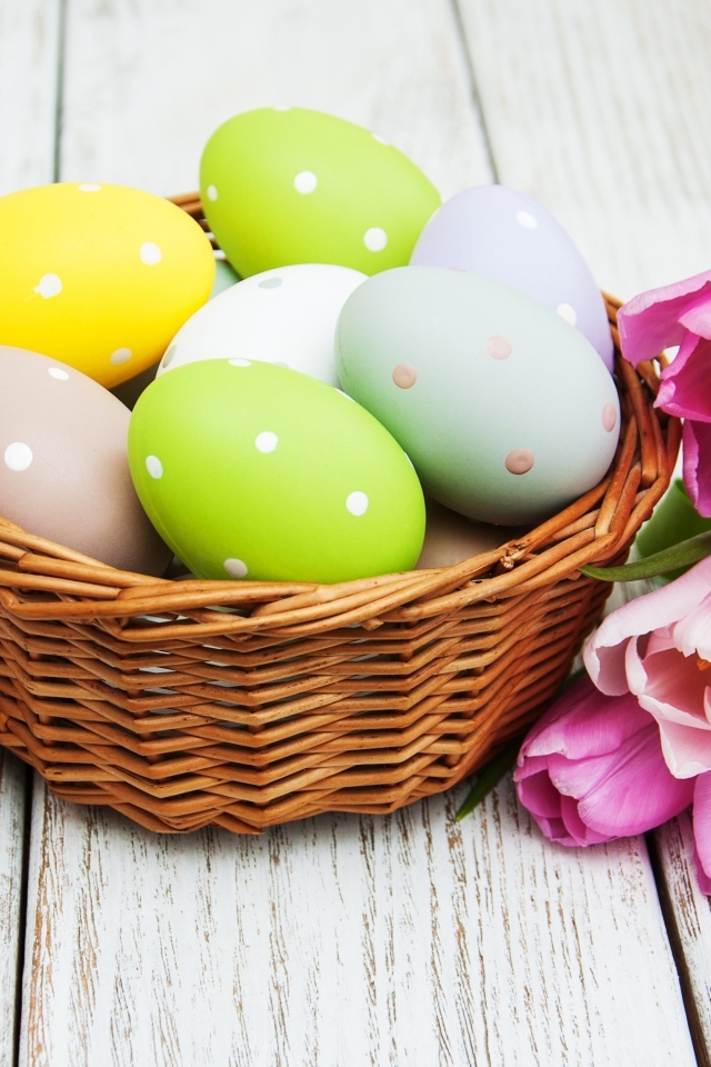 Корзина разноцветных яиц с тюльпанами на столе на Пасху