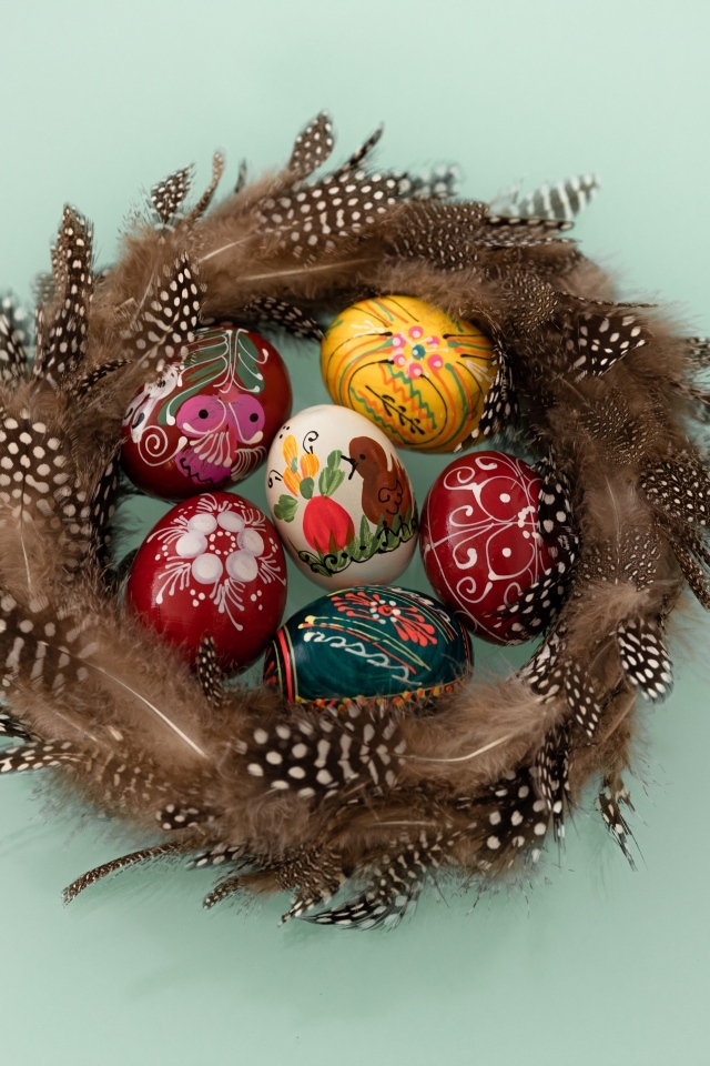 Красивые разноцветные яйца в гнезде из перьев на сером фоне