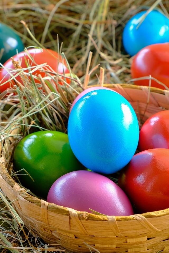 Разноцветные пасхальные яйца в корзине на сене