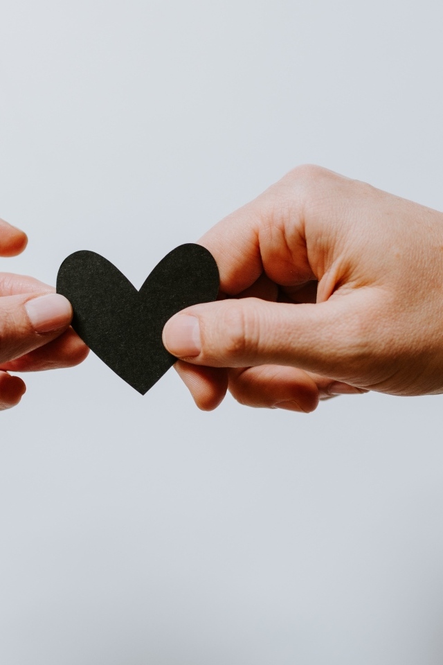 Черное бумажное сердце в руках на сером фоне