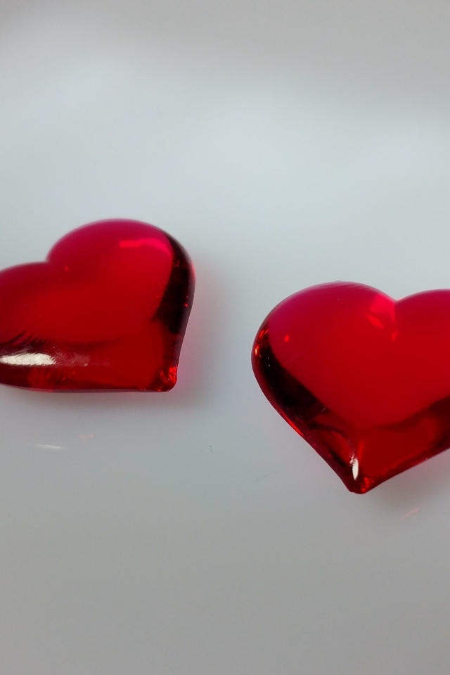 Два красных стеклянных сердца на сером фоне