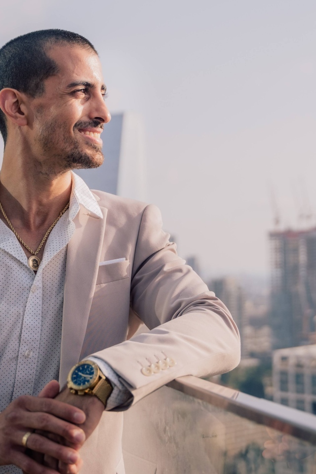 Улыбающийся стильный мужчина в костюме стоит на балконе 