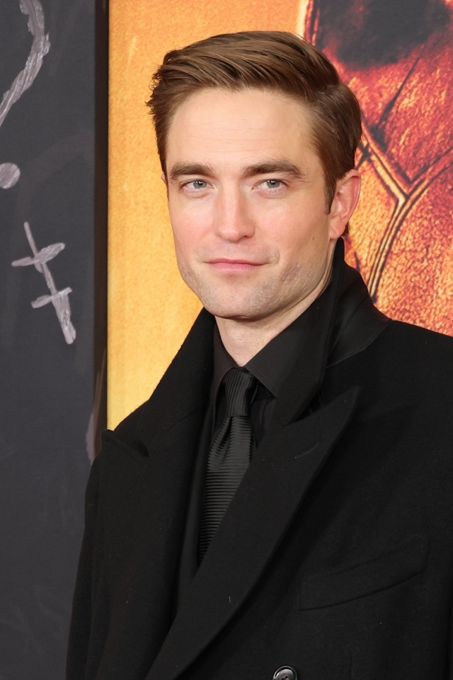 Популярный актер Роберт Паттинсон в костюме стоит у стены