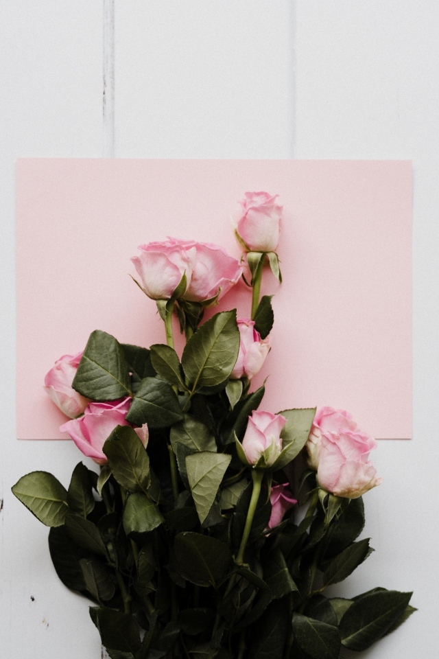 Букет роз с розовым листом бумаги на столе