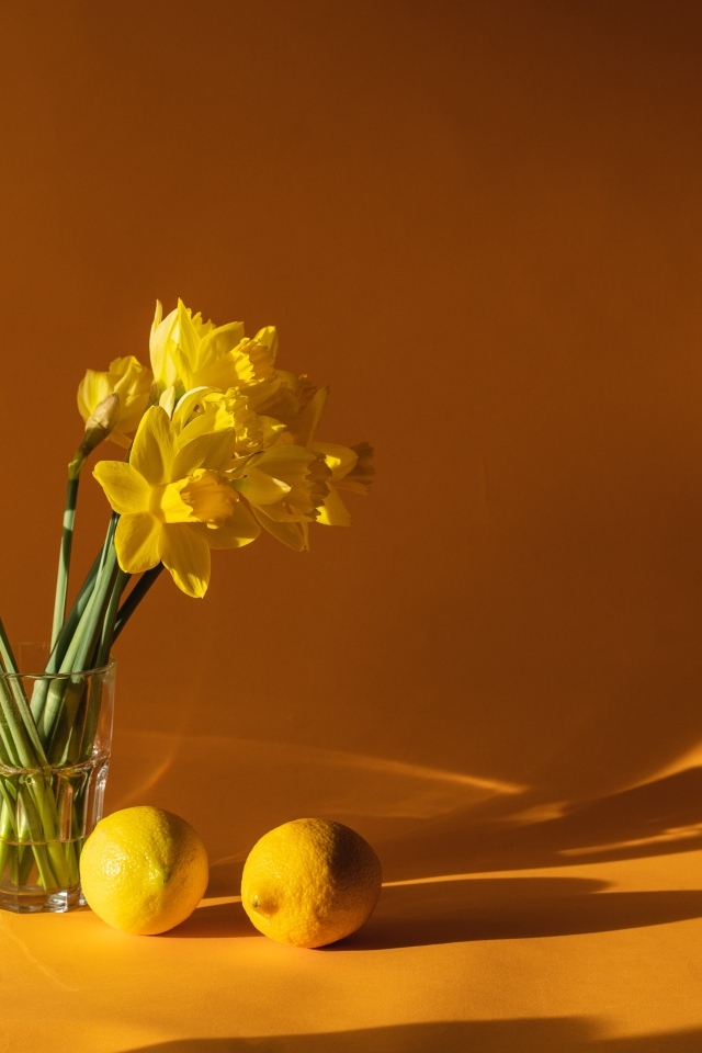 Букет желтых нарциссов в вазе на столе с лимонами