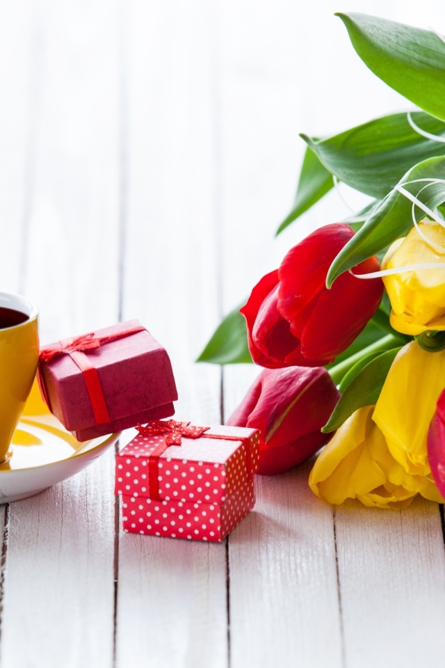Желтая чашка кофе на столе с подарками и букетом тюльпанов