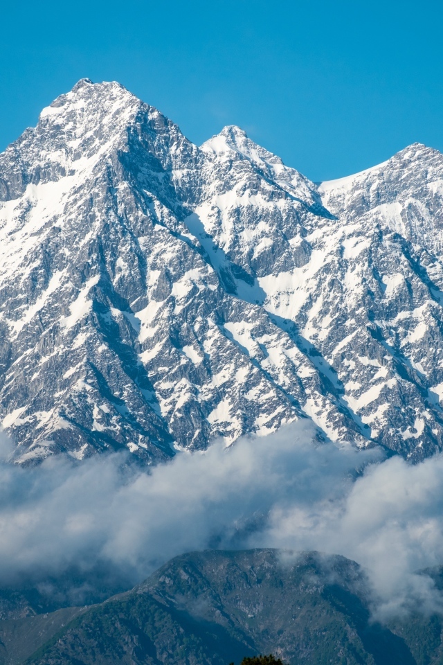 Высокие заснеженные горы в тумане под голубым небом