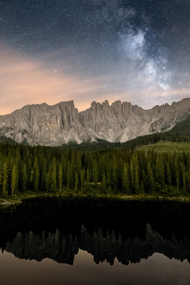 Млечный путь над горами и лесом отражающимися в воде