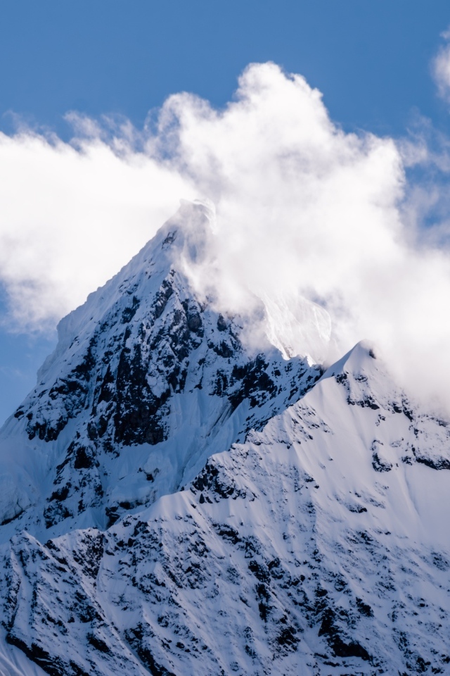 Острая заснеженная вершина горы в белых облаках