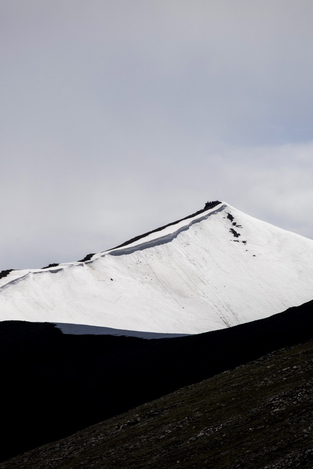 Заснеженная вершина горы под грозовым небом