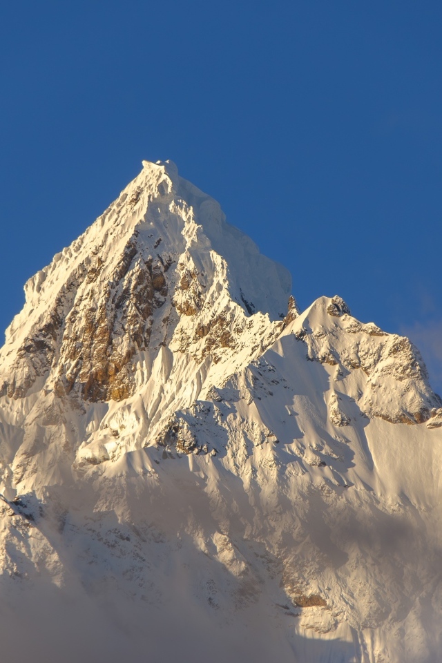 Крутая заснеженная вершина горы на голубом фоне