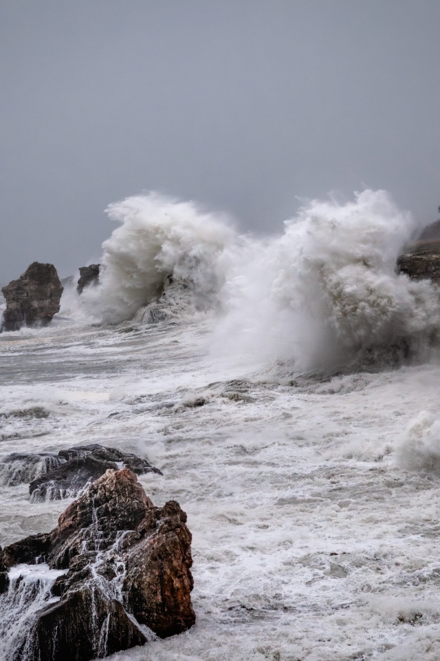 Белые пенные волны бьются об камни во время шторма