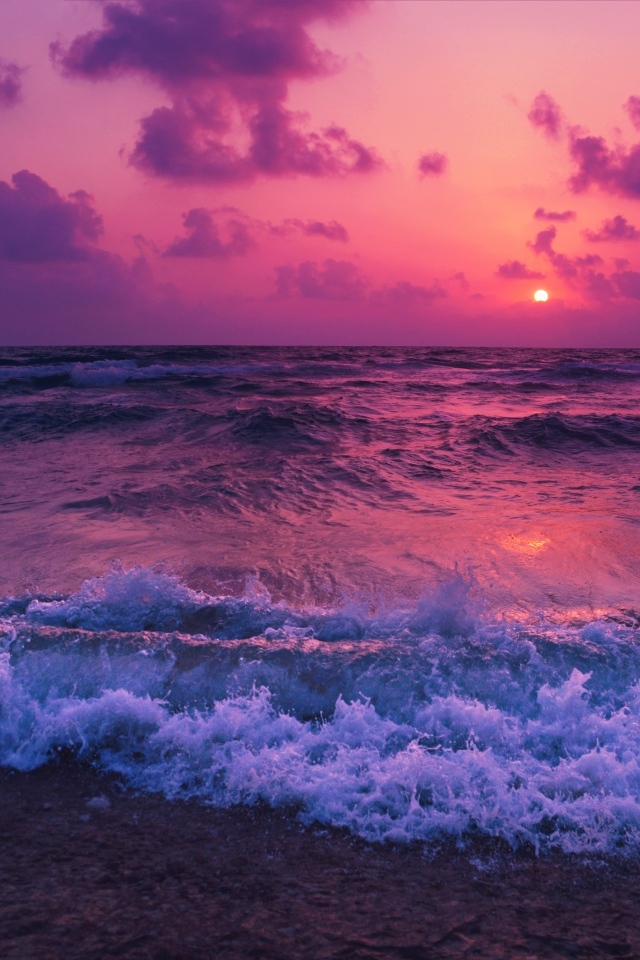 Белые морские волны на берегу в лучах розового заката