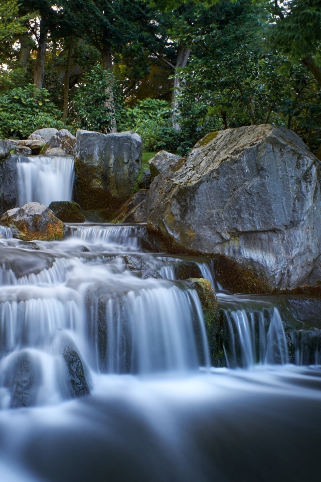 Водопад стекает по большим холодным камням в лесу