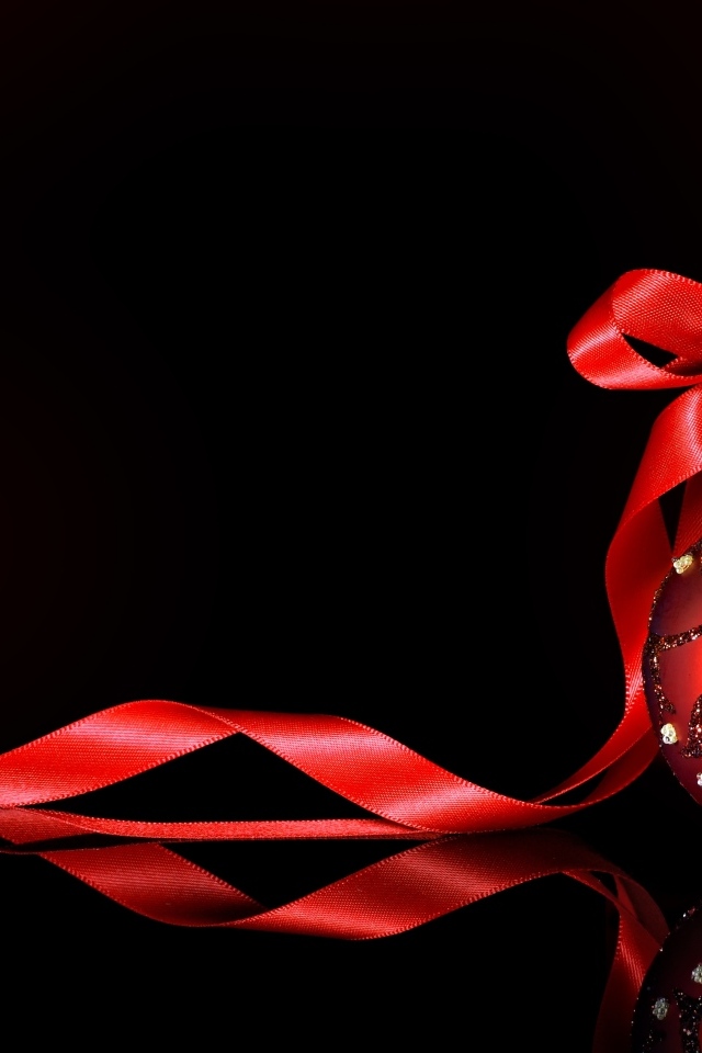 Красный елочный шар с лентой на черном фоне