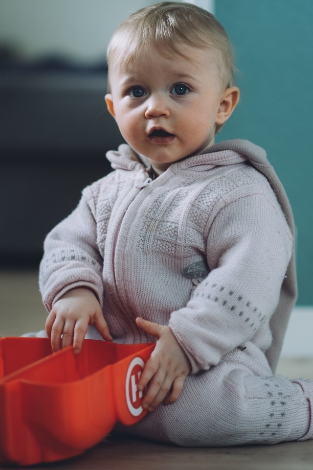 Маленький мальчик в теплом костюме сидит на полу