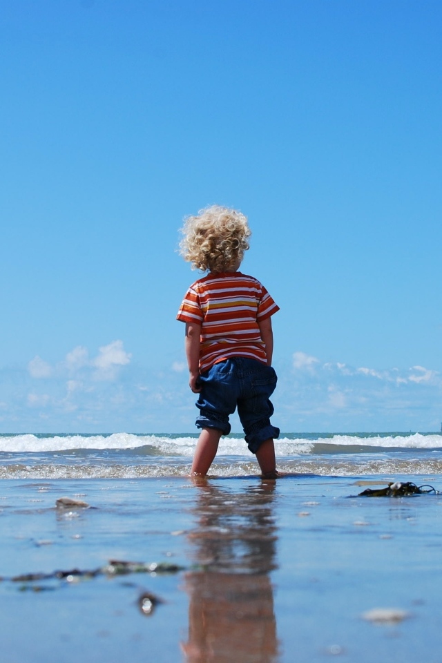 Маленький мальчик гуляет по мокрому песку у моря